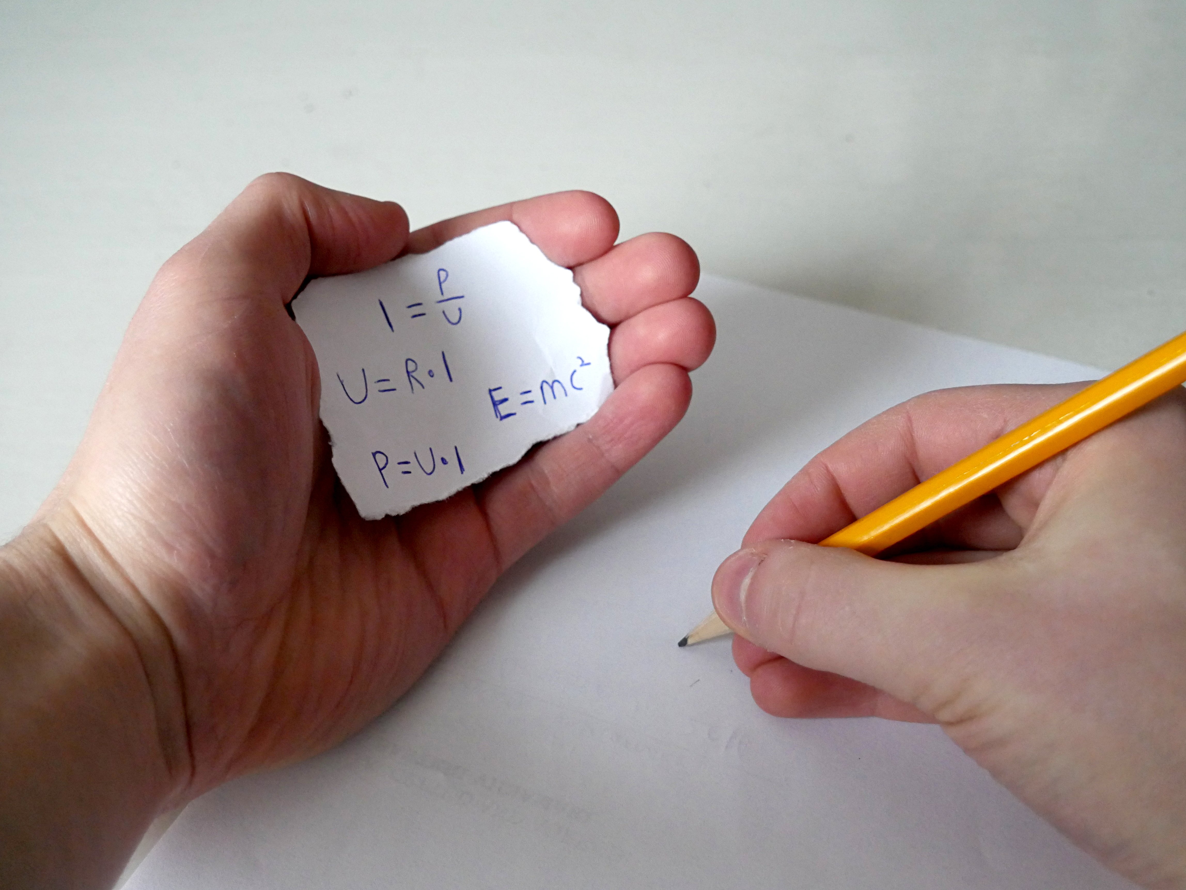 La imagen muestra una nota escondida en el hueco de la mano mientras se realiza un examen.