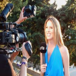 La imagen muestra a una reportera con un micrófono en la mano hablando a una cámara de televisión.