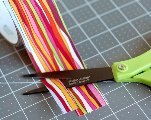 La imagen muestra unas tijeras a punto de cortar una cinta de colores.