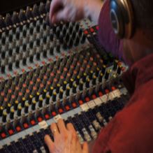 La imagen muestra las manos de una persona tocando una mesa de mezclas de sonido.
