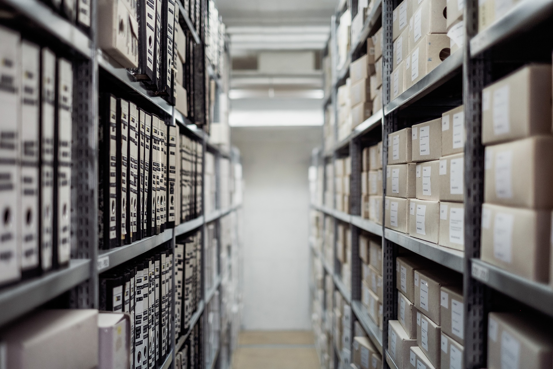 La imagen muestra un pasillo de un almacén con estanterías a ambos lados llenas de archivadores definitivos