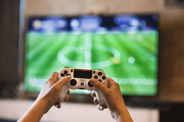 La imagen muestra una pantalla con vídeo juego de fútbol y una persona jugando.