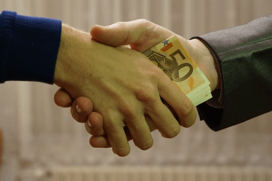 La imagen muestra una mano dando dinero a otra