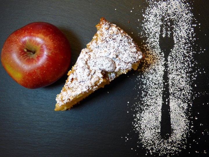 La imagen muestra una manzana roja y un trozo de tarta sobre una mesa.
