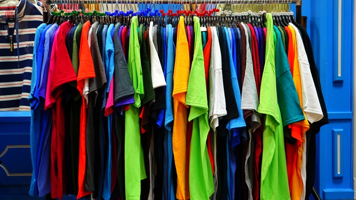 La imagen muestra un perchero lleno de camisetas en una tienda