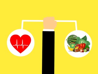 La imagen muestra una mano sosteniendo una balanza con un corazón latiendo a un lado y un numeroso grupo de frutas y verduras al otro.
