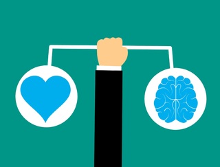 La imagen muestra una mano sosteniendo una balanza con un corazón a un lado y un cerebro al otro.