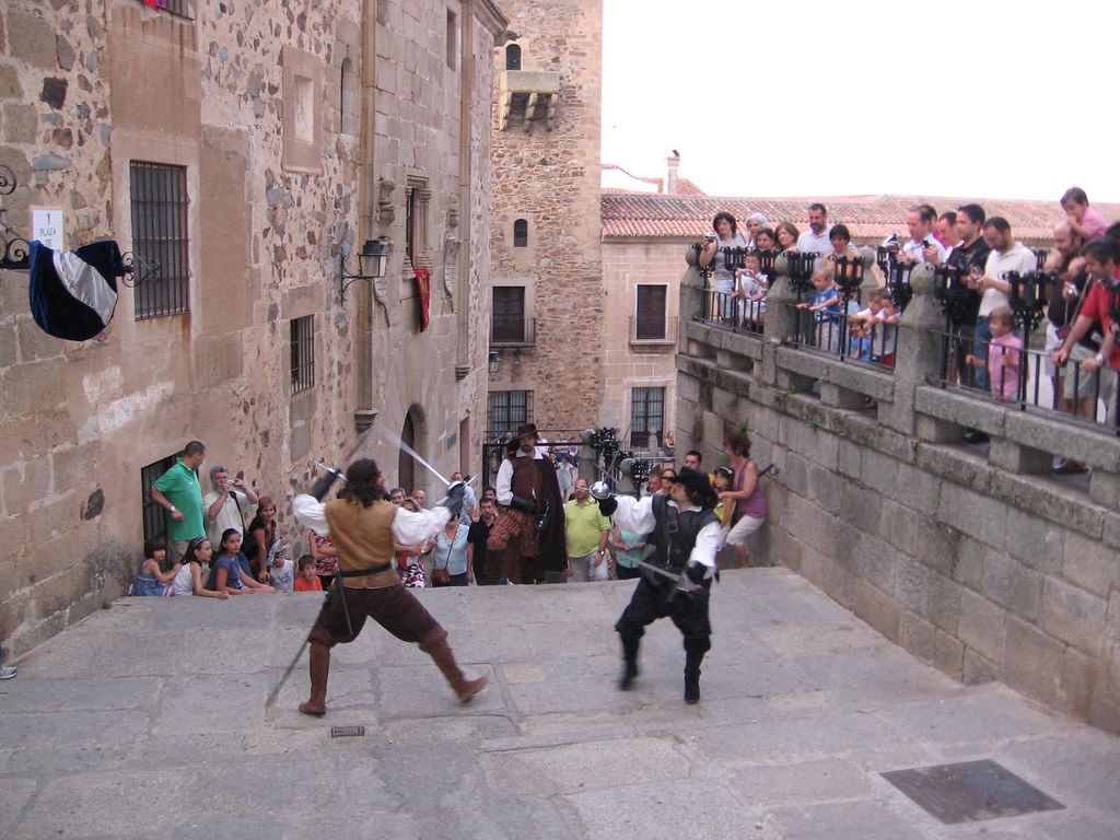 Swashbuckling La imagen muestra a dos personas luchando con las espadas en la calle mientras el público lo observa.