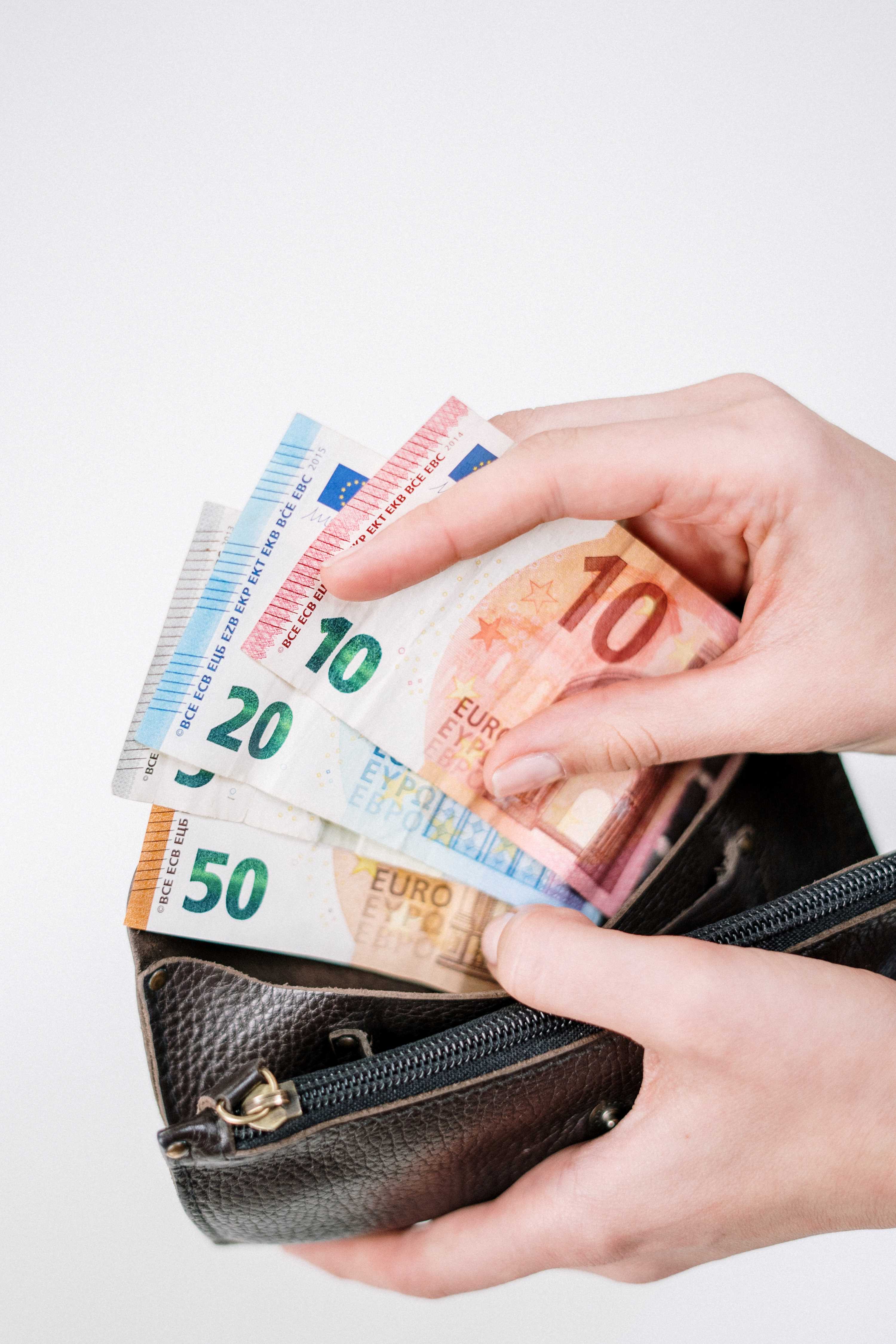 La imagen muestra una cartera abierta con una mano extrayendo varios billetes de euros.