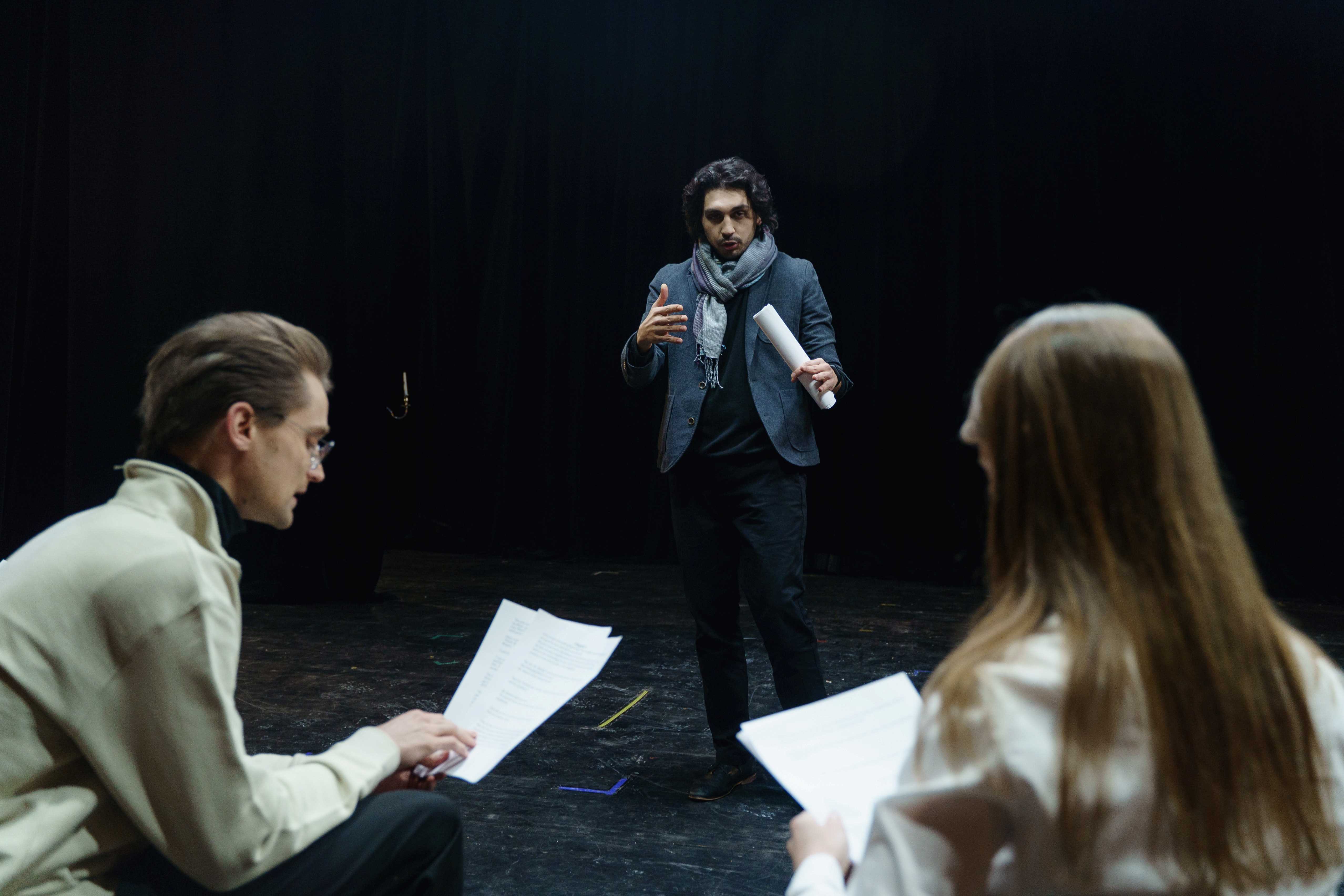 La imagen muestra unos actores sosteniendo un guion durante un ensayo.