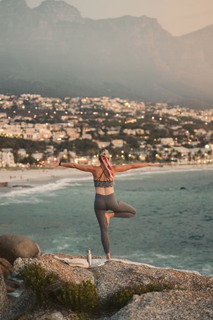 La imagen muestra una persona haciendo una postura de yoga mirando al mar.