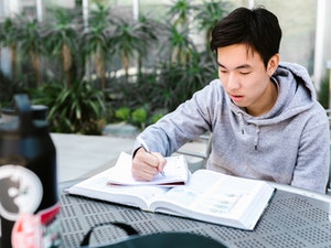 La imagen muestra un chico escribiendo un cuaderno