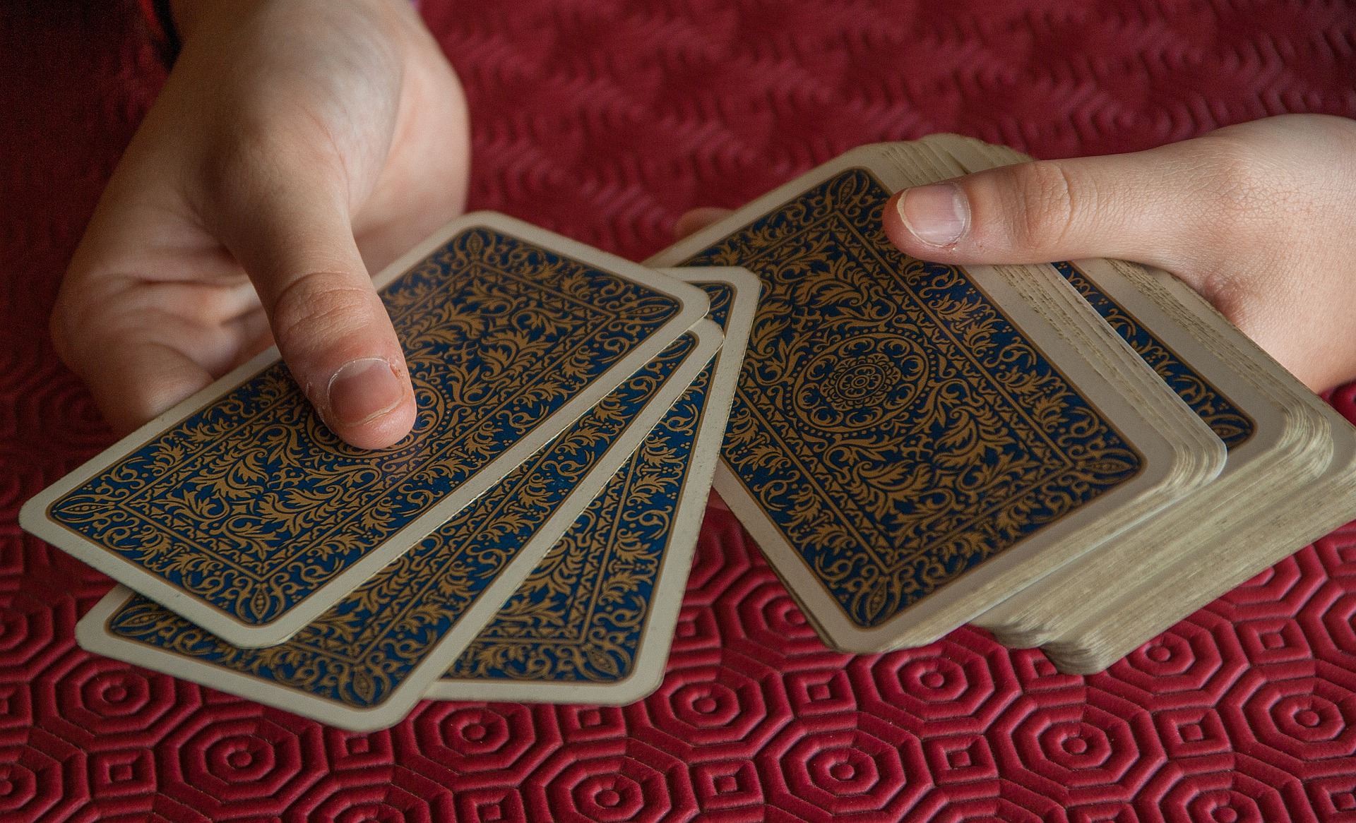 Encima de un tapete rojo unas manos reparten cartas de una baraja