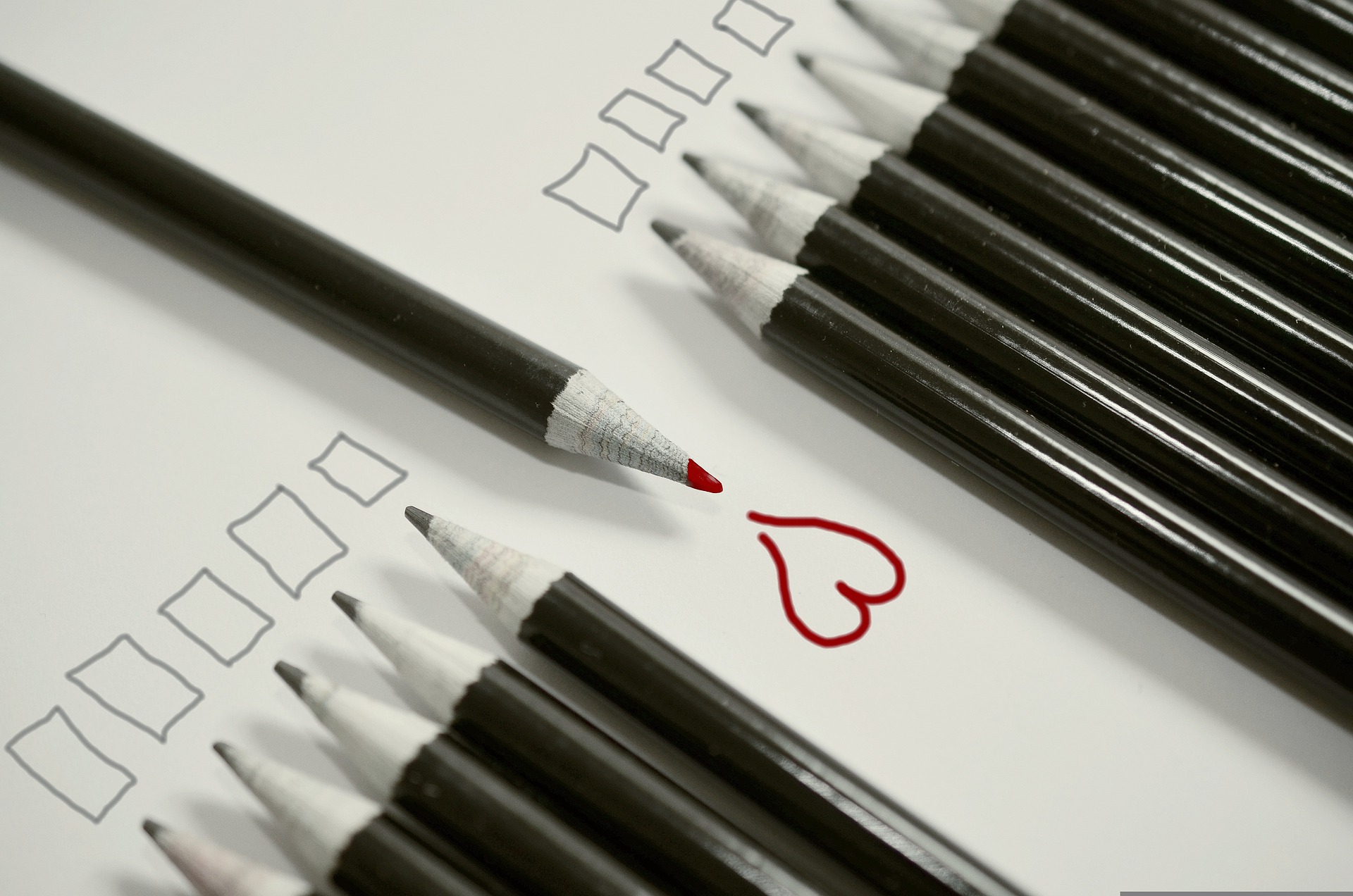 Toda una fila de lápices negros señalan a unos cuadrados que supuestamente han escrito. En el centro de la fila irrumpe en dirección contraria un lápiz rojo señalando a un corazón rojo que supuestamente ha escrito ese lápiz rojo.
