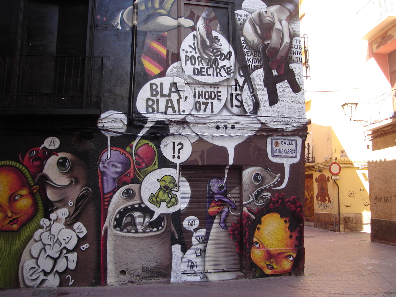La imagen muestra un mural sobre una pared y una puerta, en el cual hay varios personajes irreales similares a pequeños monstruos, cada uno de los cuales tiene varios bocadillos de texto