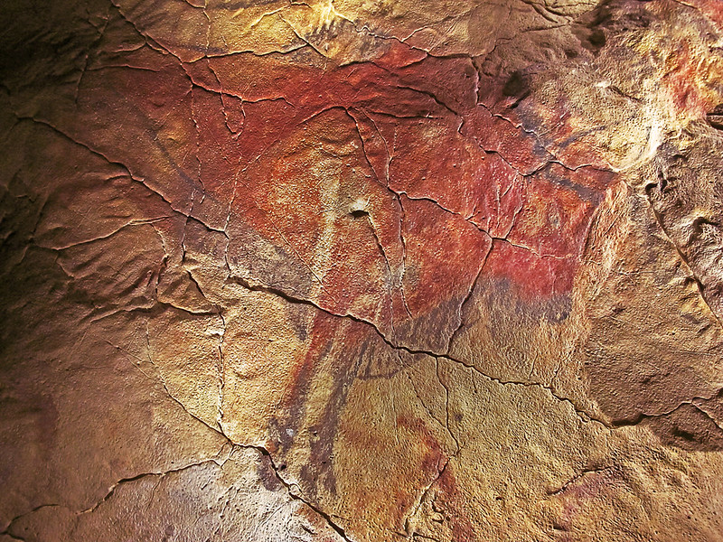 La imagen muestra pinturas rupestres de color rojo sobre un muro de piedra en la que aparece un animal similar a un bisonte