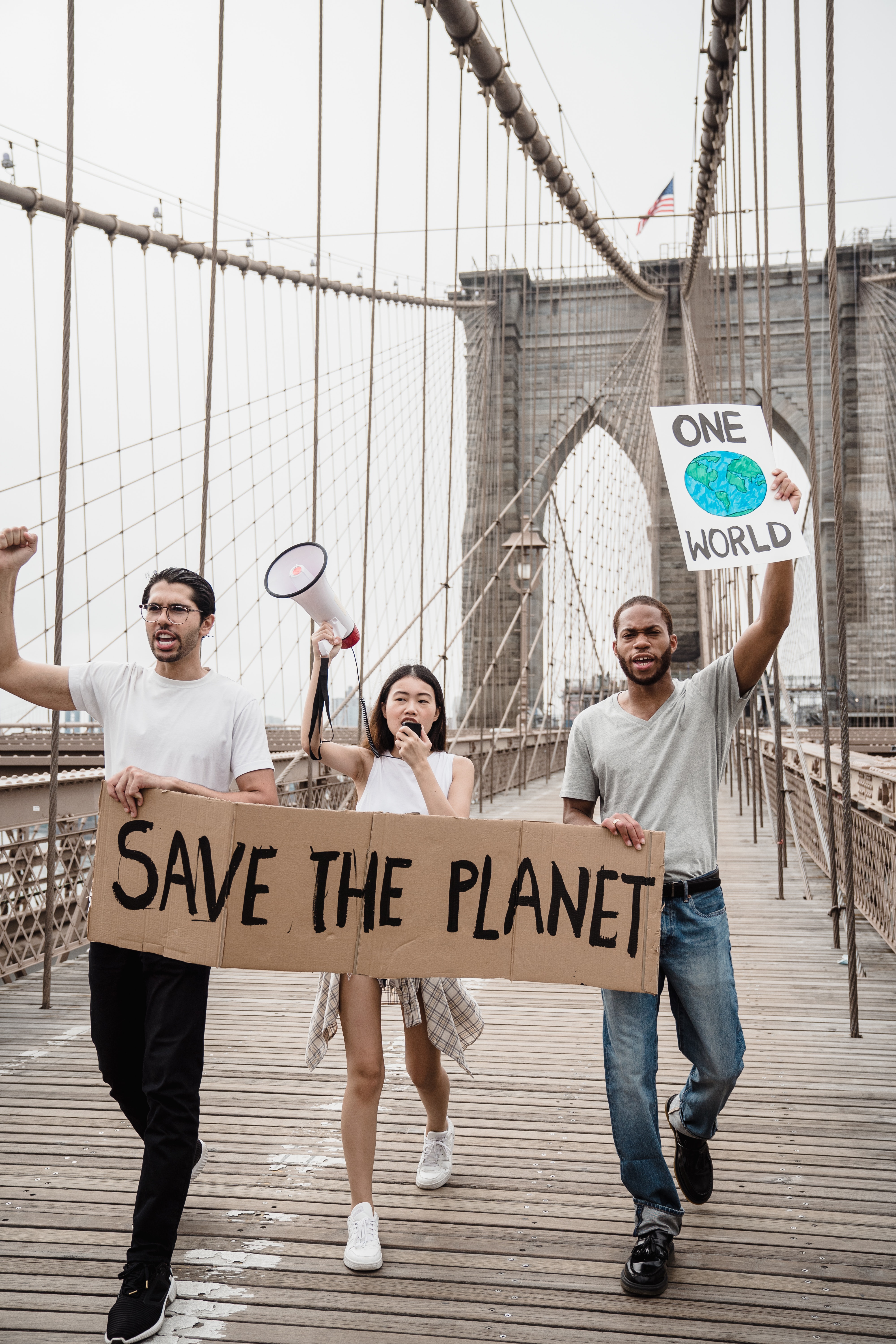 Dos hombres y una mujer caminando sobre un puente con carteles a favor de salvar y cuidar el planeta