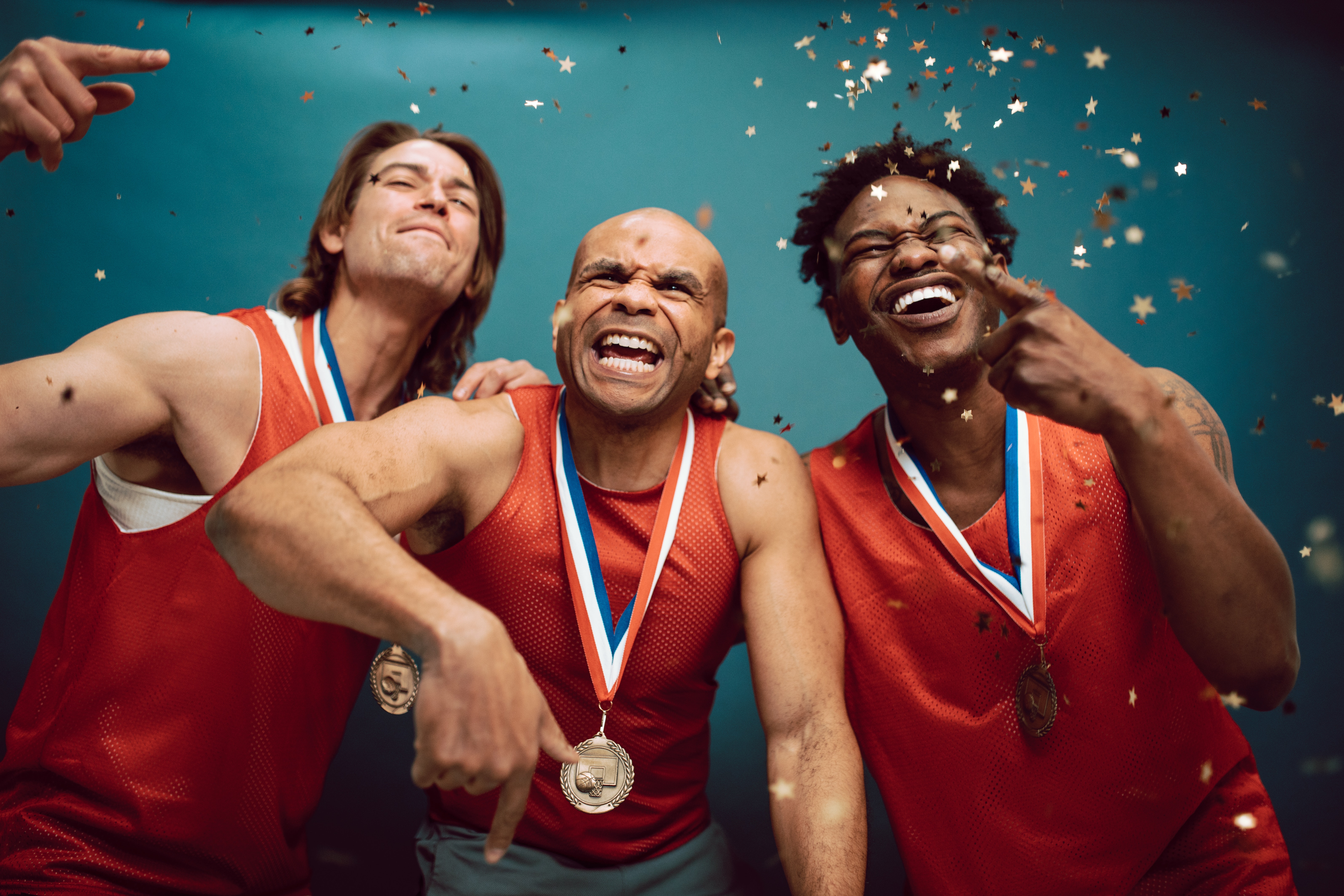 La imagen muestra tres personas alegres con ropa deportiva y medallas con gesto de celebración.