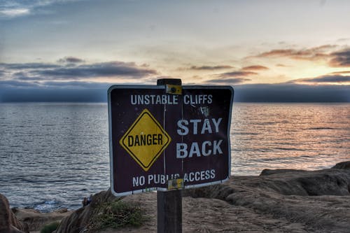 Foto de una playa en la que aparece un cartel en inglés dónde pone peligro, acantilados inestables, volver atrás.