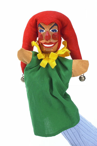 Marioneta de mano de un arlequín con sombrero rojo y vestido verde.