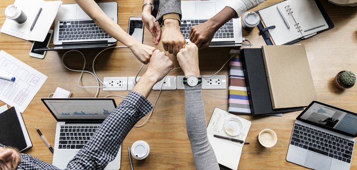 fotografía de un grupo de personas trabajando conjuntamente y que juntan sus puños como símbolo de cooperación