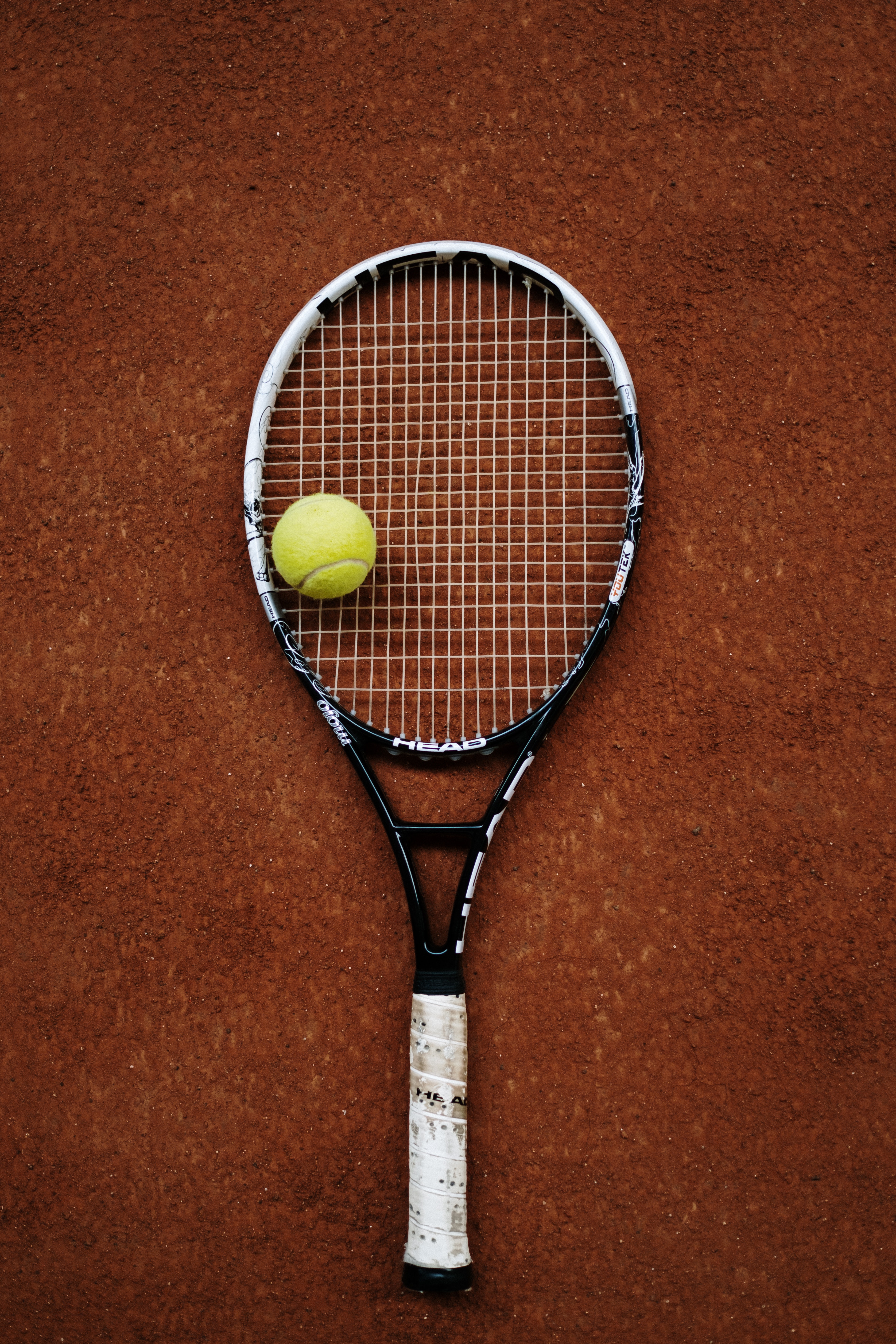 Raqueta de tenis posada sobre tierra batida con una pelota encima