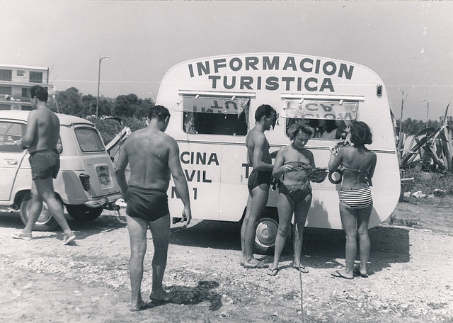 Oficina móvil de información turística. Gente en bañador consultando en una oficina de información turística móvil en los años 60