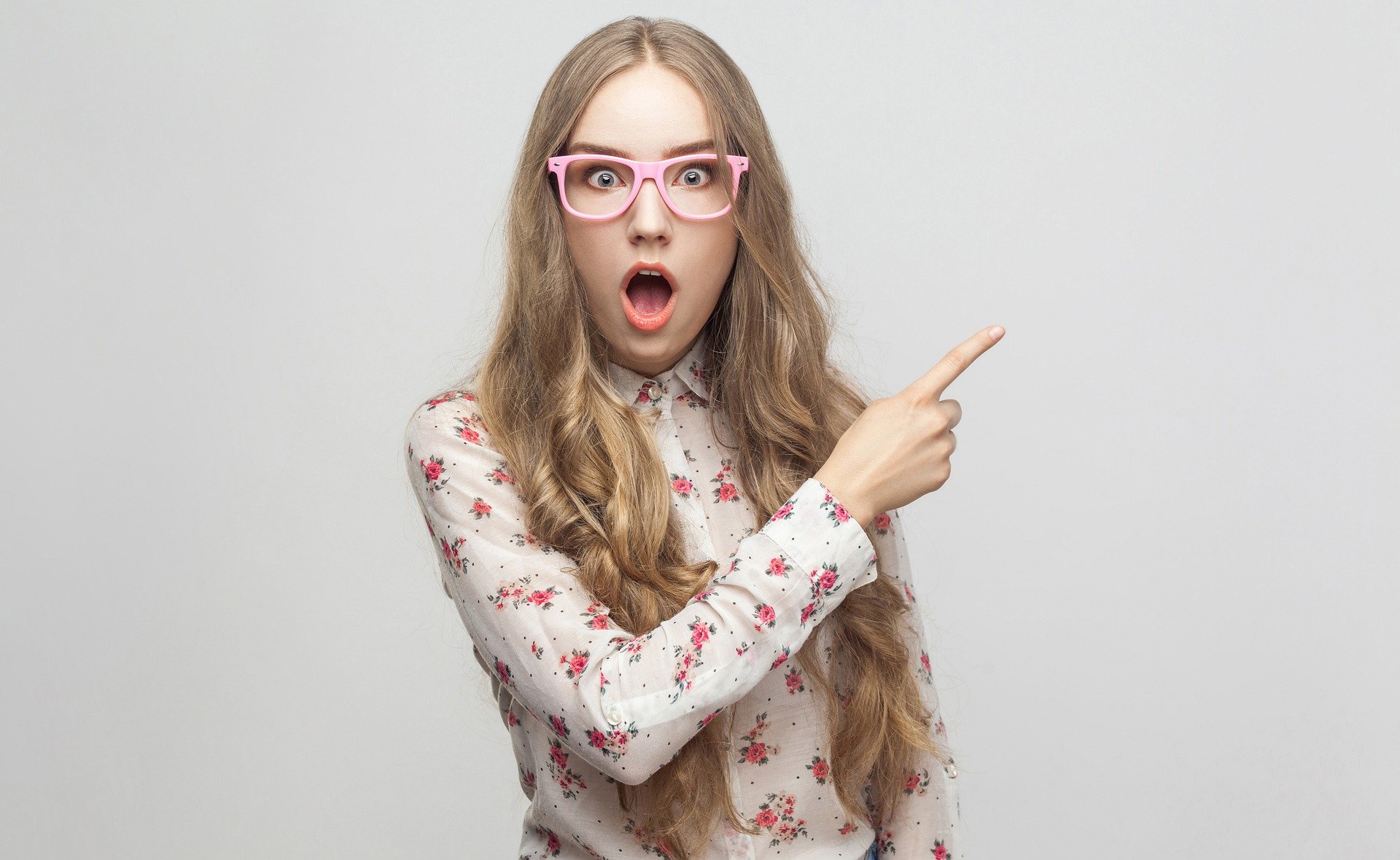 Chica con gafas asombrada y señalando hacia arriba