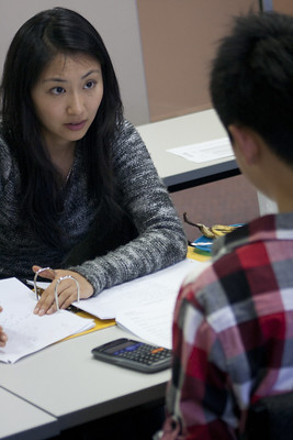 La imagen muestra a una profesora sentada frente a un alumno al que explica algo.