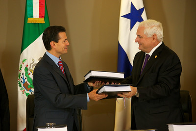 La imagen muestra a dos señores con traje que se intercambian un mismo documento.