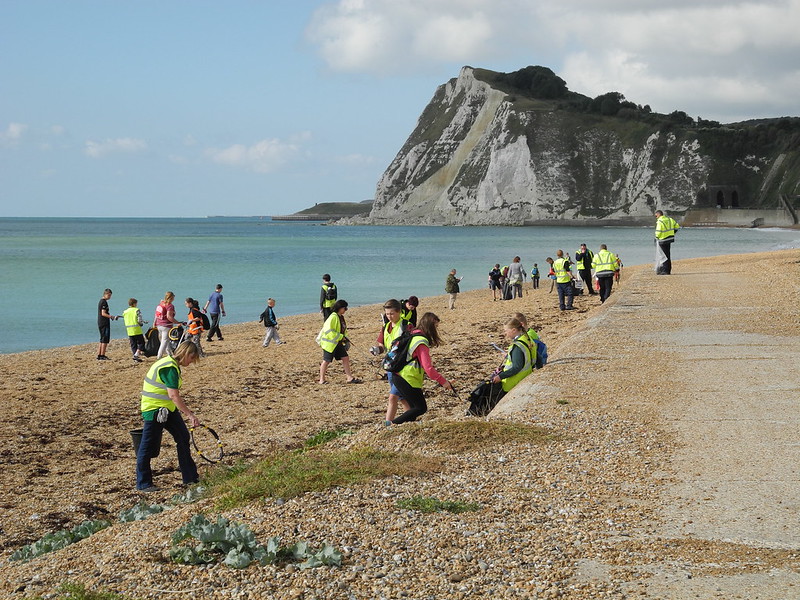La imagen muestra a un grupo de voluntarios con cestas y bolsas que limpian una playa.