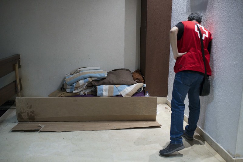 La imagen muestra a un voluntario que observa las mantas y cartones en los que duerme una persona sin hogar.