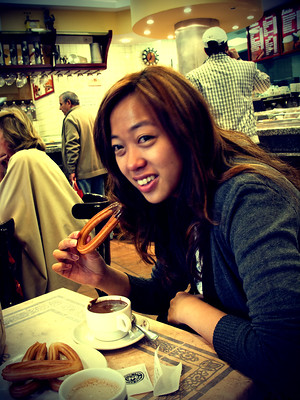La imagen muestra a una chica en pleno acto de comer un churro mojado en chocolate.
