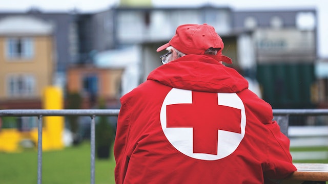 La imagen muestra la imagen de un hombre de espaldas con ropa de la Cruz Roja.