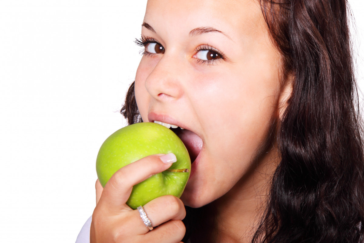 La imagen muestra una niña comiendo una manzana.