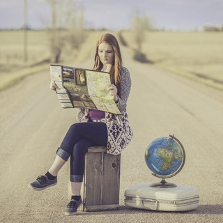 fotografía de una chica sentada sobre su maleta en mitad de una carretera con un mapa en la mano y junto a ella un globo terráqueo