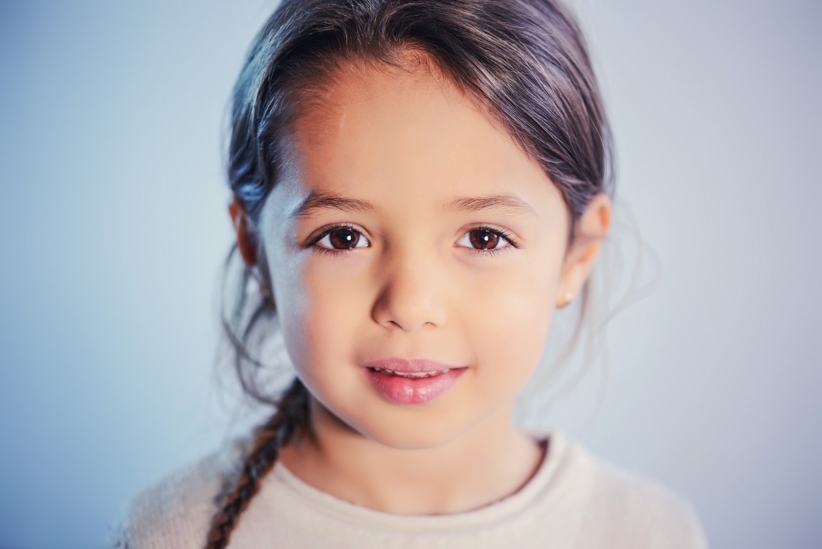 La imagen muestra una niña de piel morena, pelo largo y castaño oscuro, ojos marrones y labios gruesos