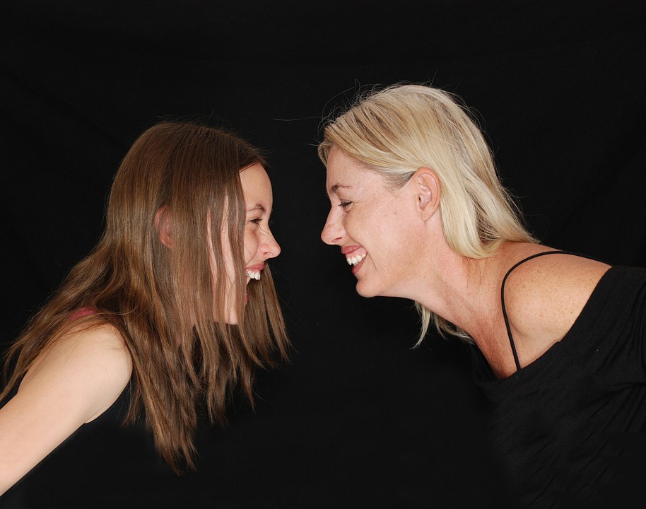 La imagen muestra dos niñas rubias de piel clara mirándose y riendo