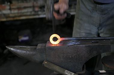Herrero trabajando una pieza de metal al rojo sobre un yunque.