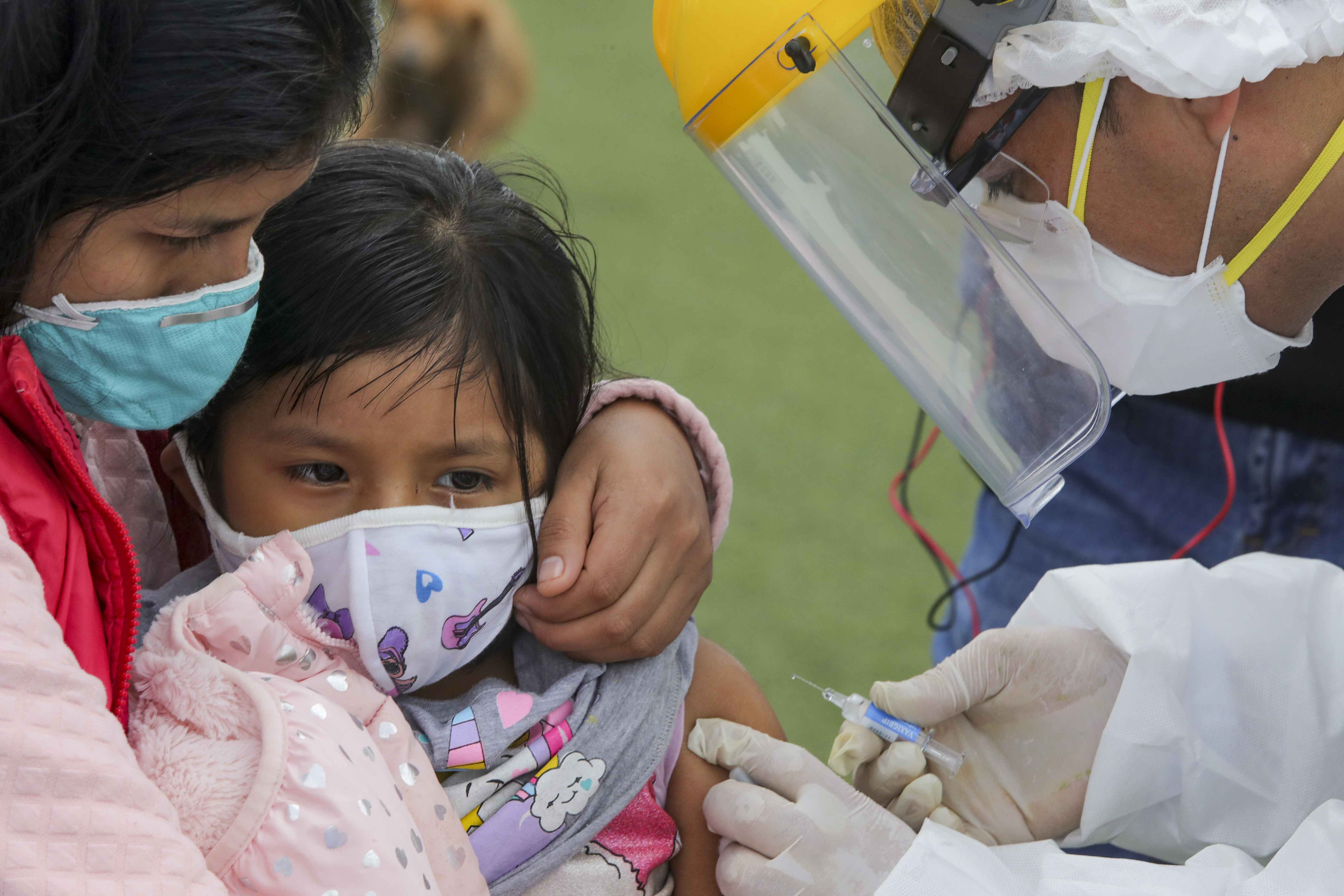 La imagen muestra una niña en brazos de su brazo con una enfermedad y un hombre poniéndole una vacuna en el brazo. 