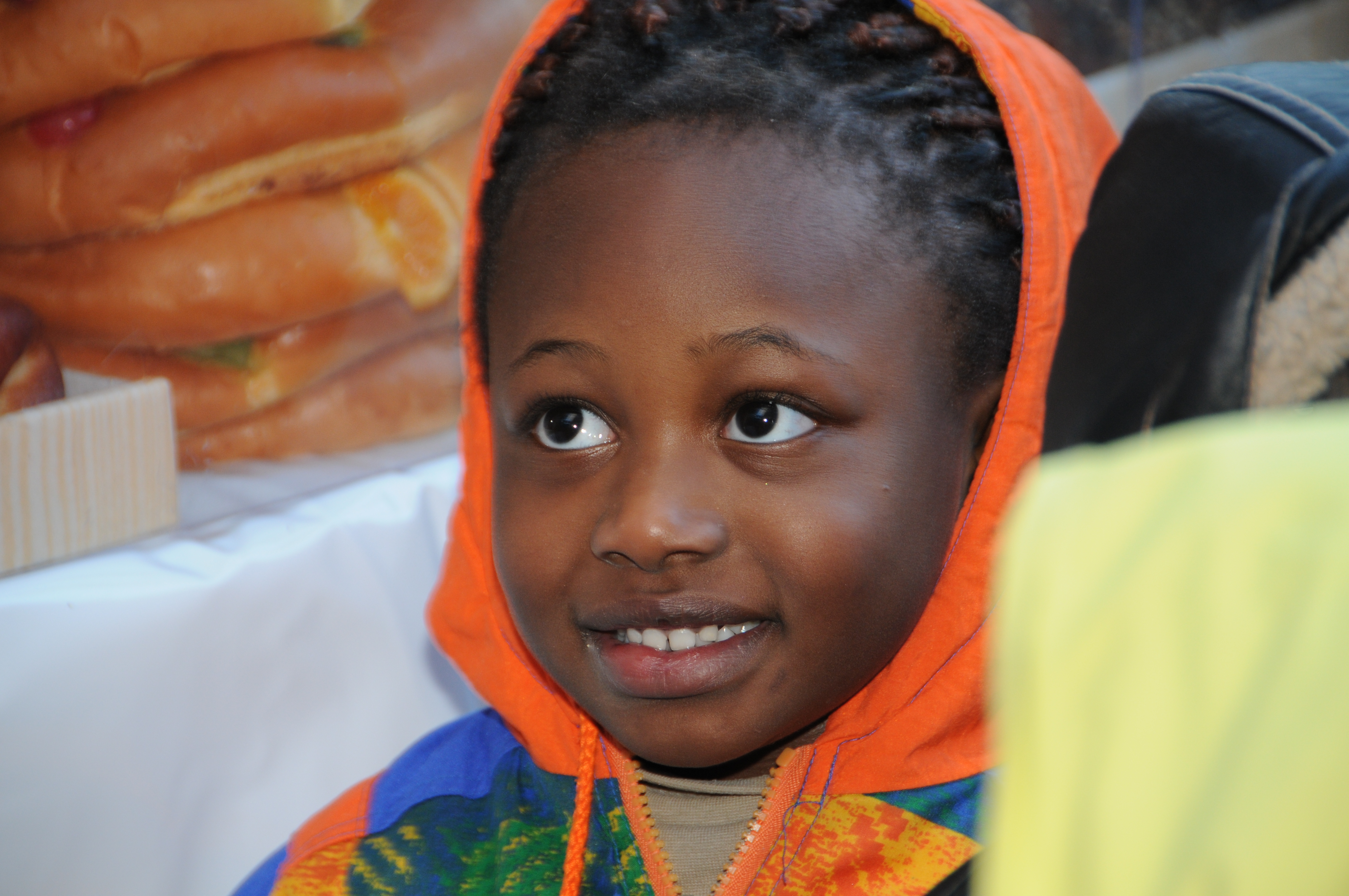 La imagen muestra un niño negrito sonriendo con una  chaqueta naranja.