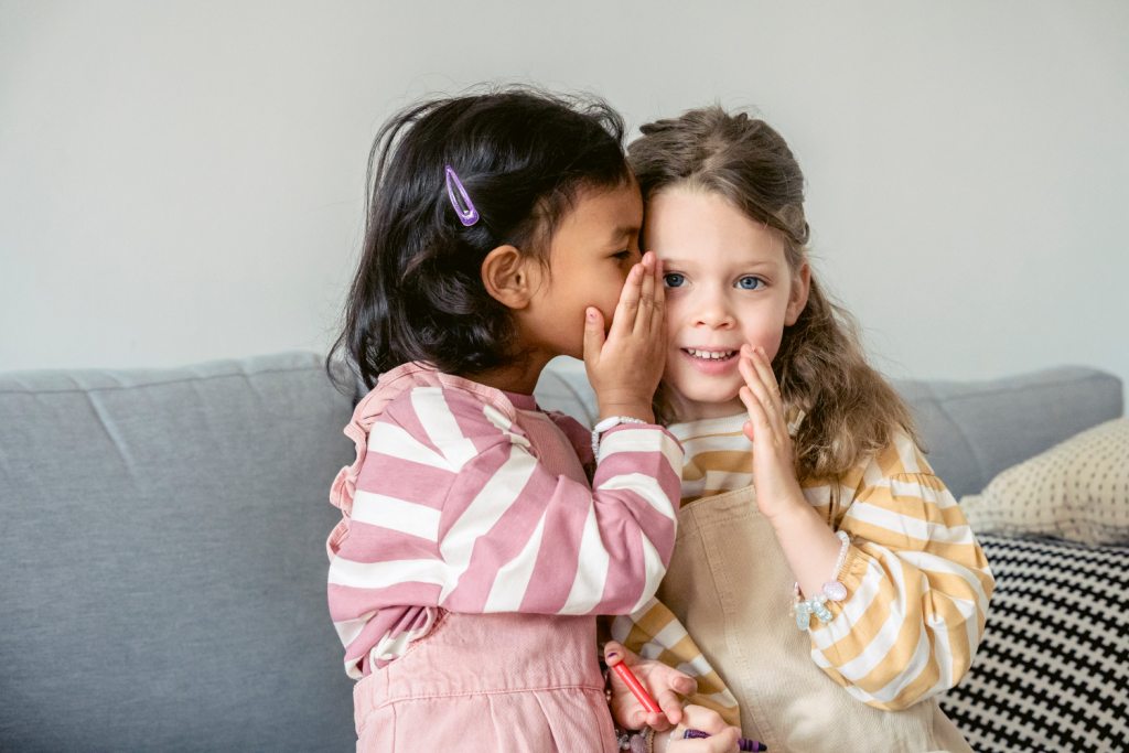 La imagen muestra una niña contándole a otra niña un secreto.