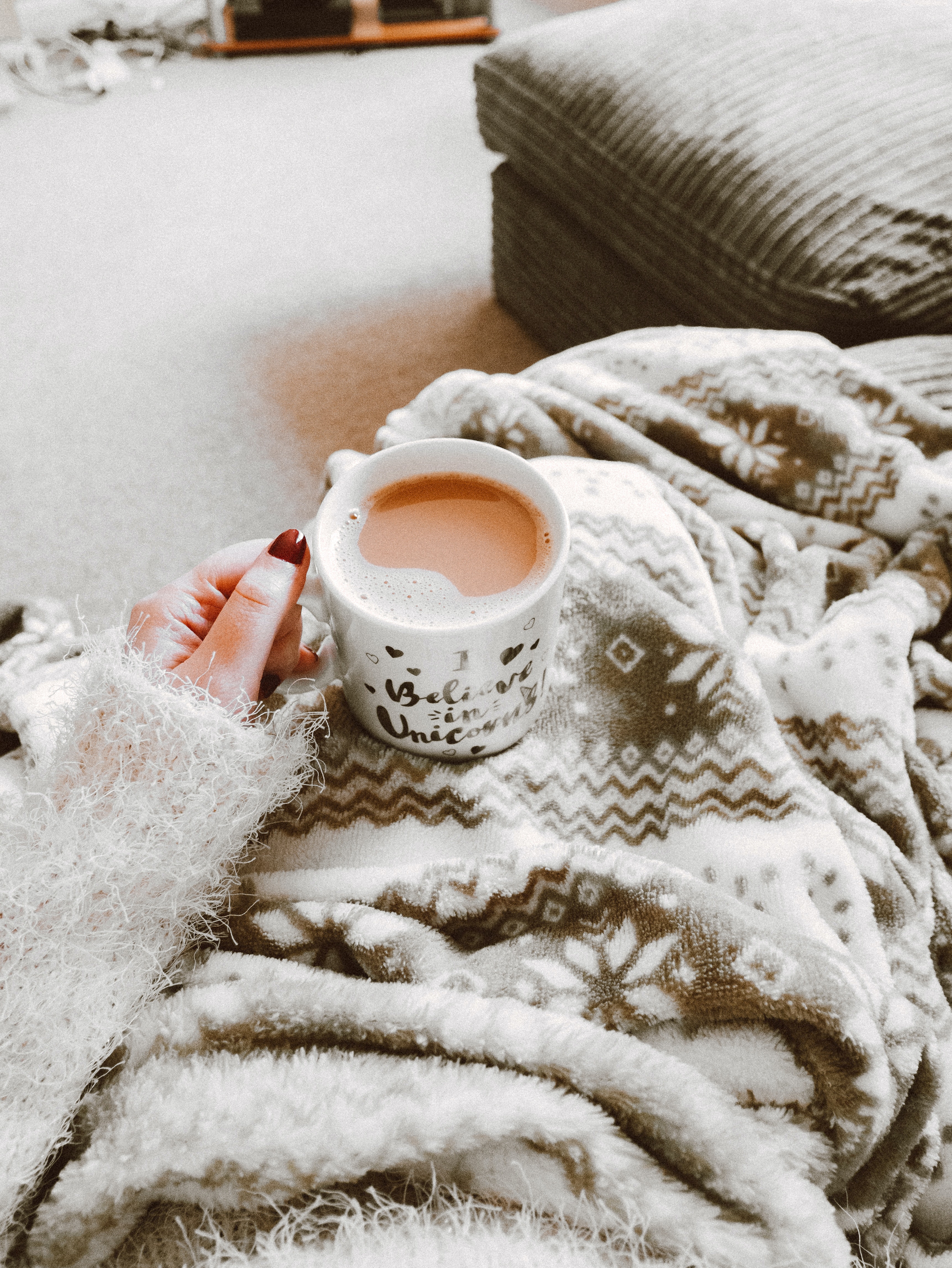 La imagen muestra una cálida escena con manta y un café.