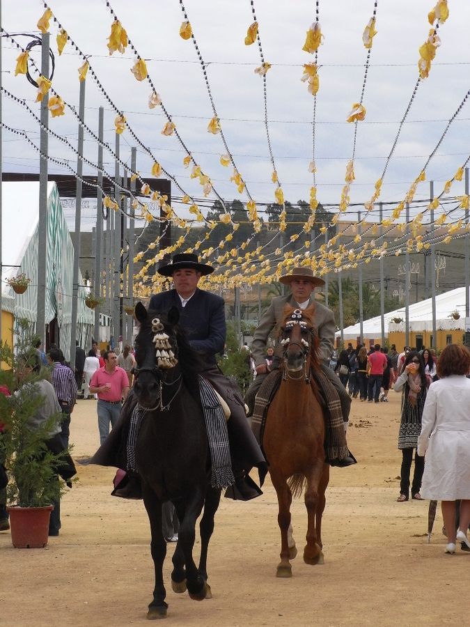 Dos hombres montados a caballo en la feria.