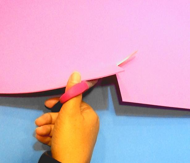 La imagen muestra una mano recortando una plancha de goma eva rosa