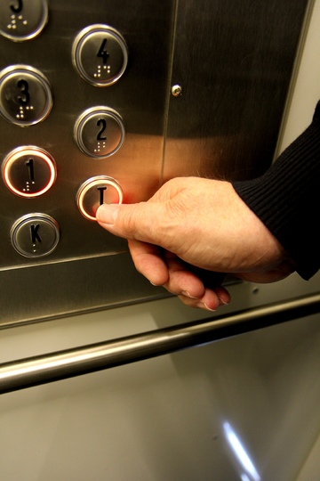 La imagen muestra un dedo tocando los botones de un ascensor.