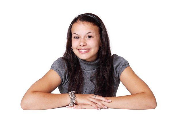 La imagen muestra una chica sonriente con los brazos sobre la mesa.