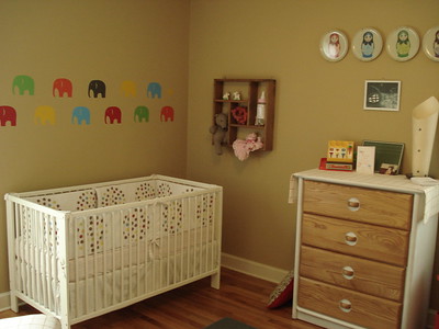 La imagen muestra una habitación de bebé, con cona, cómoda y decoración infantil. 