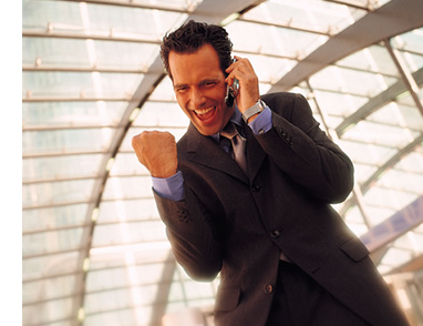 La imagen muestra una persona vestida con traje que está hablando por el teléfono móvil mientras sonríe y levanta el puño.