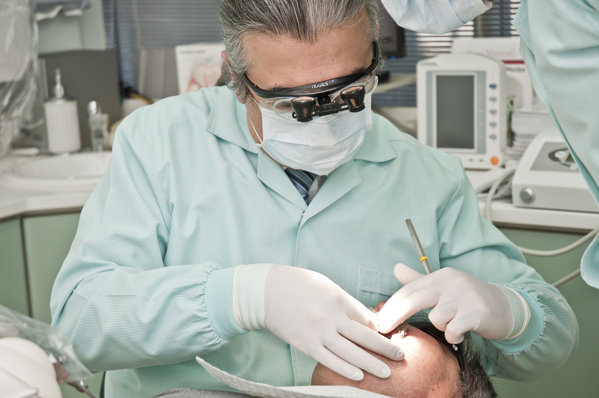 Un dentista con gafas y mascarilla está mirando los dientes de un paciente que está tumbado en la silla de una clínica dental. 